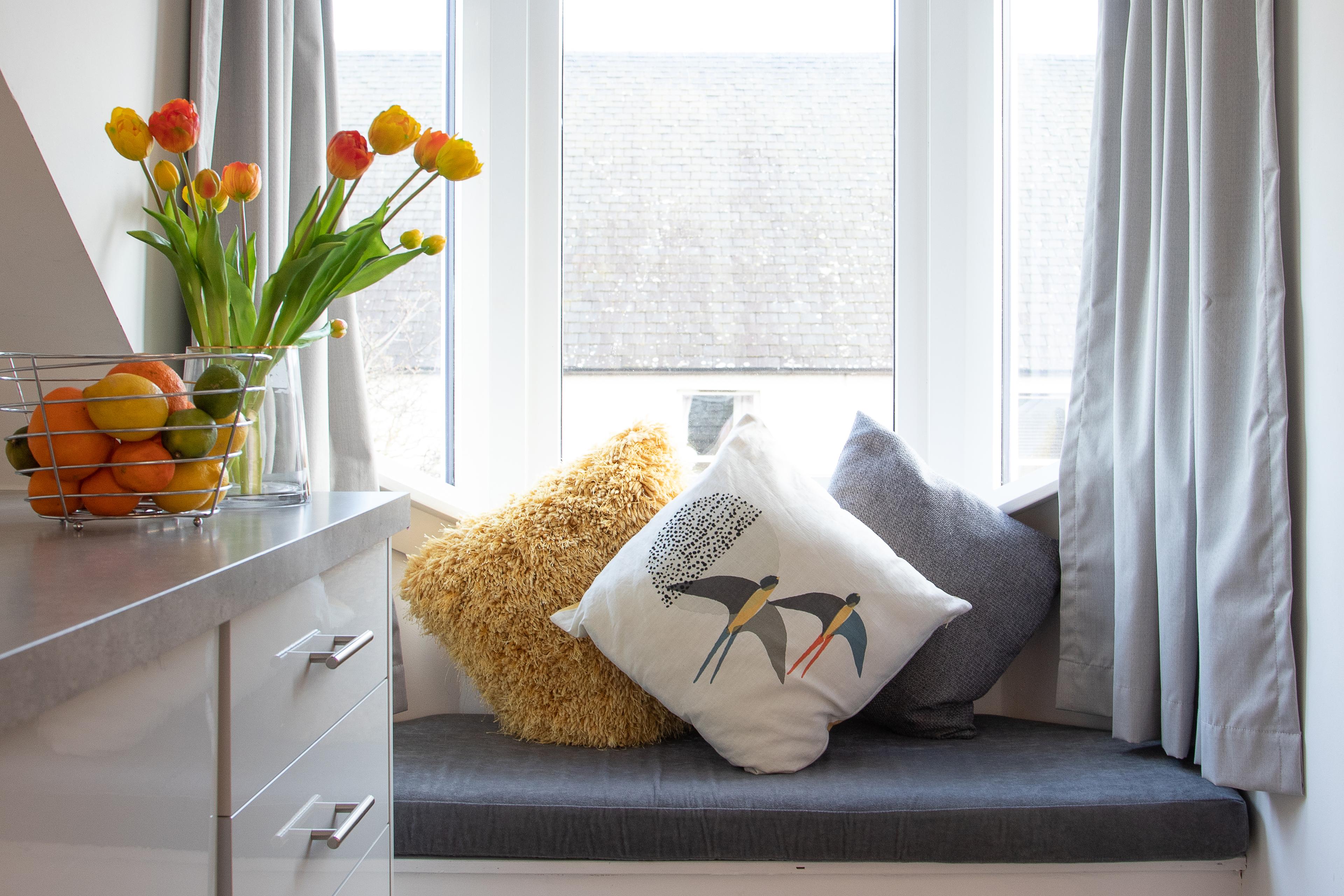 Sunny window seat with cozy cushions, fresh flowers, and charming decor