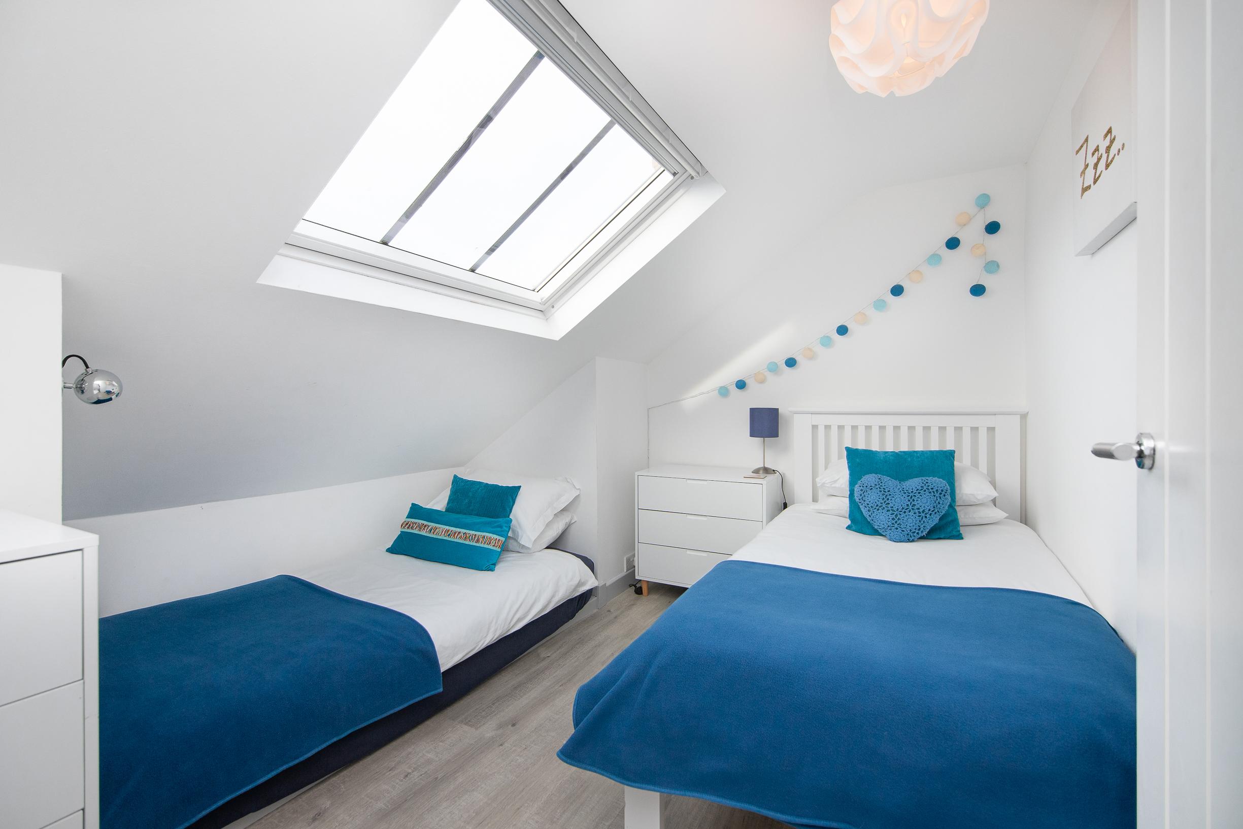 Bright twin room with skylight, cheerful blue accents, and cozy modern style
